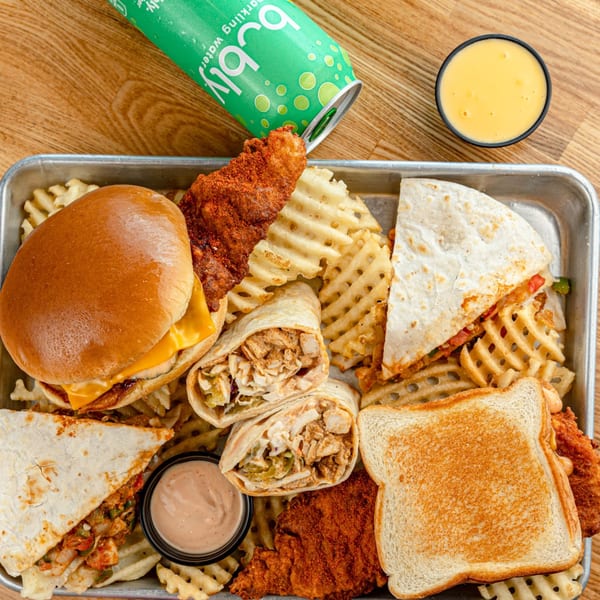 Howdy Hot Chicken platter with fried chicken, waffle fries, quesadillas, wraps, and a burger.