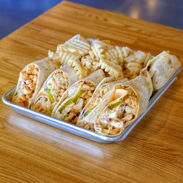 Howdy Hot Chicken wraps filled with fried chicken and waffle fries on a metal tray.