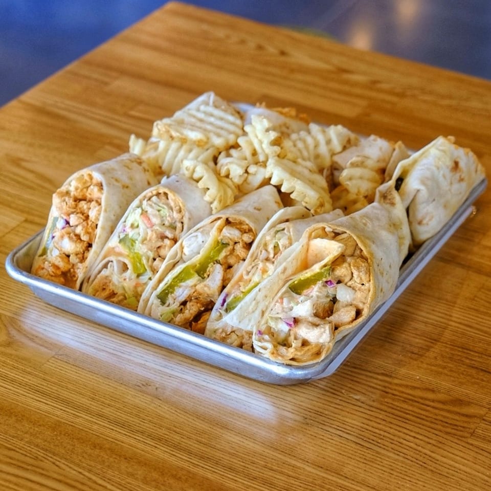 Howdy Hot Chicken wraps filled with fried chicken and waffle fries on a metal tray.