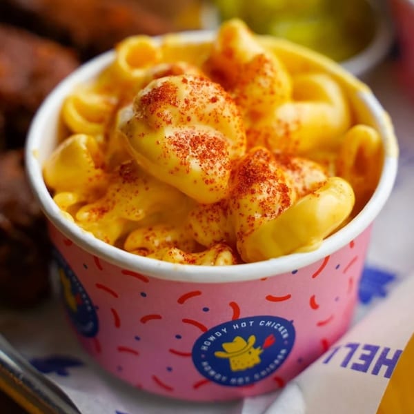 Howdy Hot Chicken's mac and cheese in a pink branded cup, topped with red seasoning.