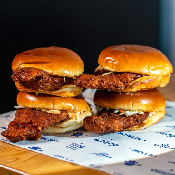 Four Howdy Hot Chicken sandwiches with crispy fried chicken, slaw, and sauce on brioche buns.