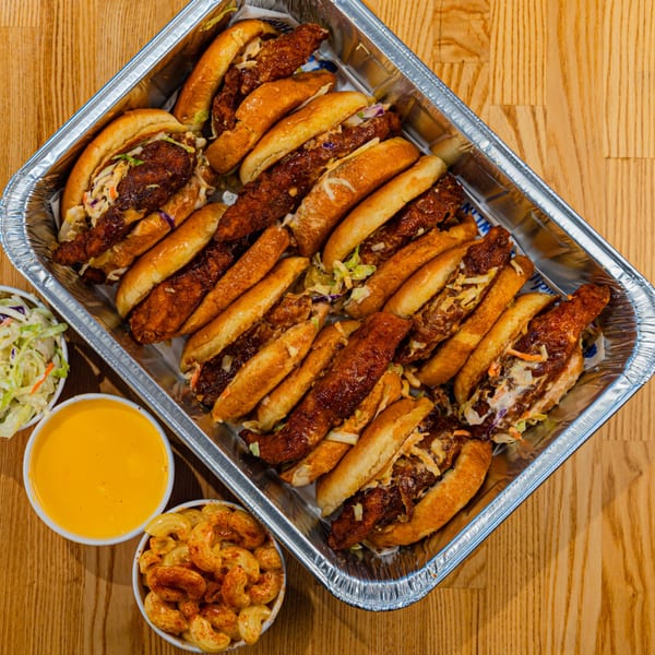 Howdy Hot Chicken sliders in a foil tray with sides of coleslaw, mac and cheese, and dipping sauce.